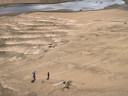 Artea Pérez y su hijo caminan bajo el sol por una playa seca de regreso a su comunidad, el 16 de octubre de 2024.