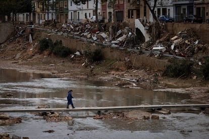 Una vecina cruza la Rambla del Poyo con un puente peatonal en Picanya (Valencia), con los márgenes del barranco llenos de escombros y destrozos, el pasado 13 de noviembre.