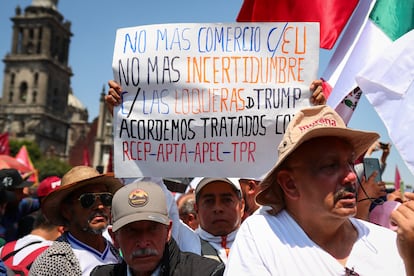 Asistentes a la asamblea en el Zócalo sostienen carteles contra los aranceles.